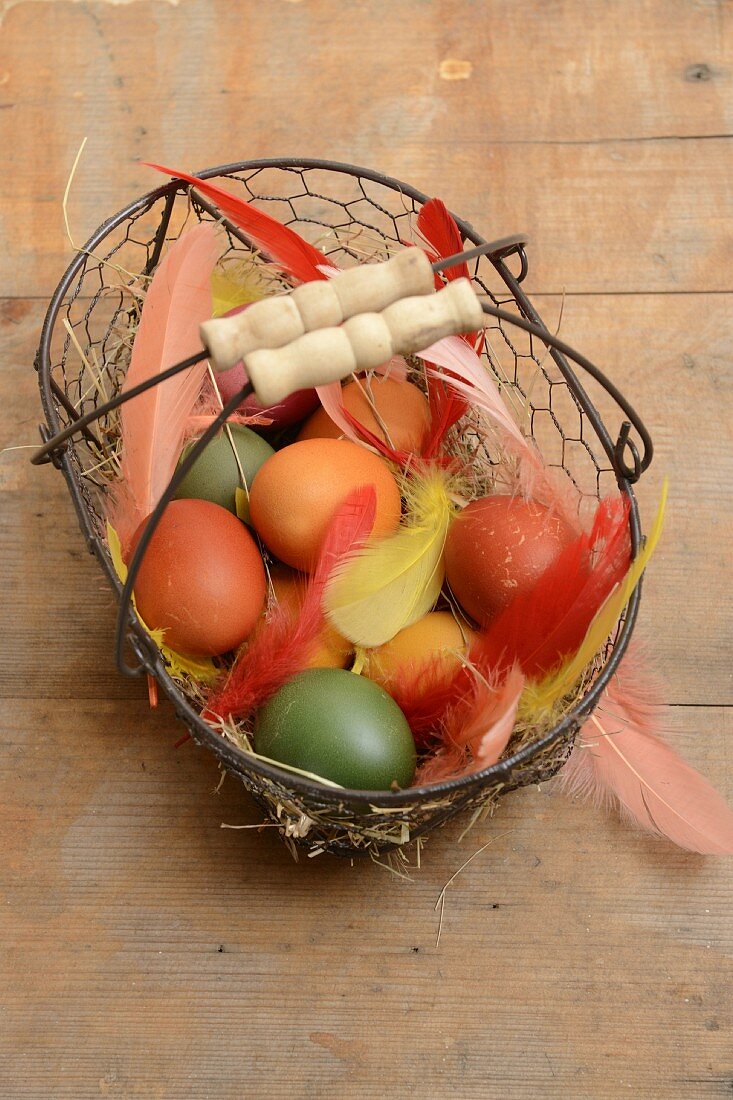 Drahtkorb mit gefärbten Eiern und Federn