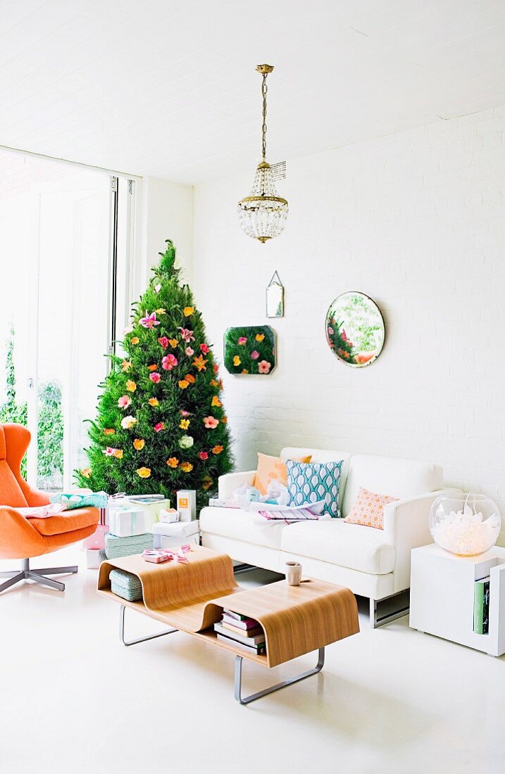Christmas tree decorated with flowers in living room with white sofa and designer coffee table
