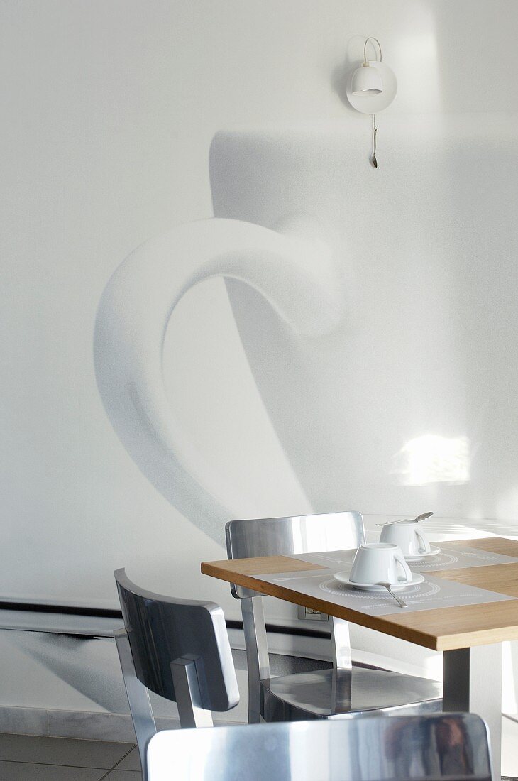 Two place settings for afternoon coffee on designer table in front of photo art with cup motif on white wall