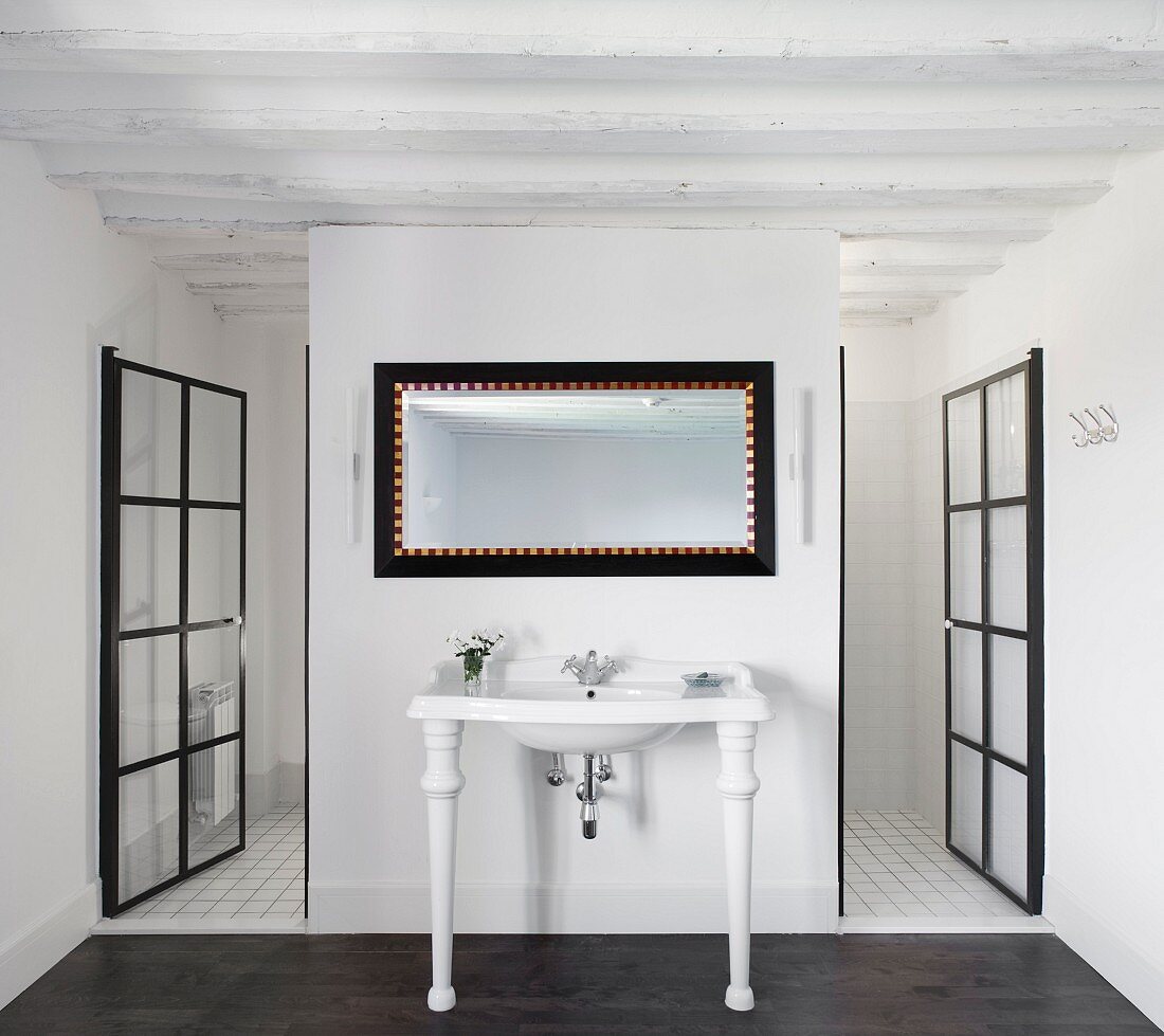 White vintage washstand against partition flanked by open glass doors with black metal lattice frames