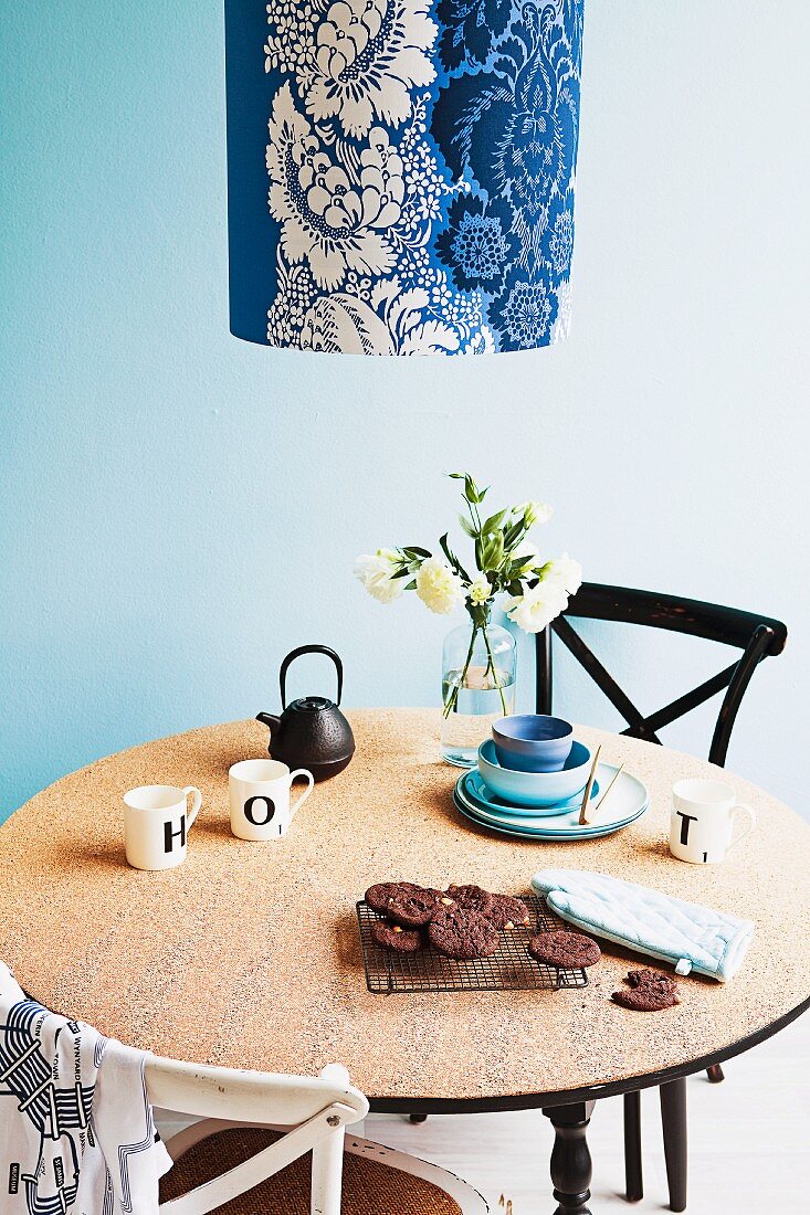 Mit aufgeklebter Korkplatte neu gestalteter Frühstückstisch, dazu Vintage Stühle und Pendelleuchte mit blauweiss floral gemustertem Stoffschirm