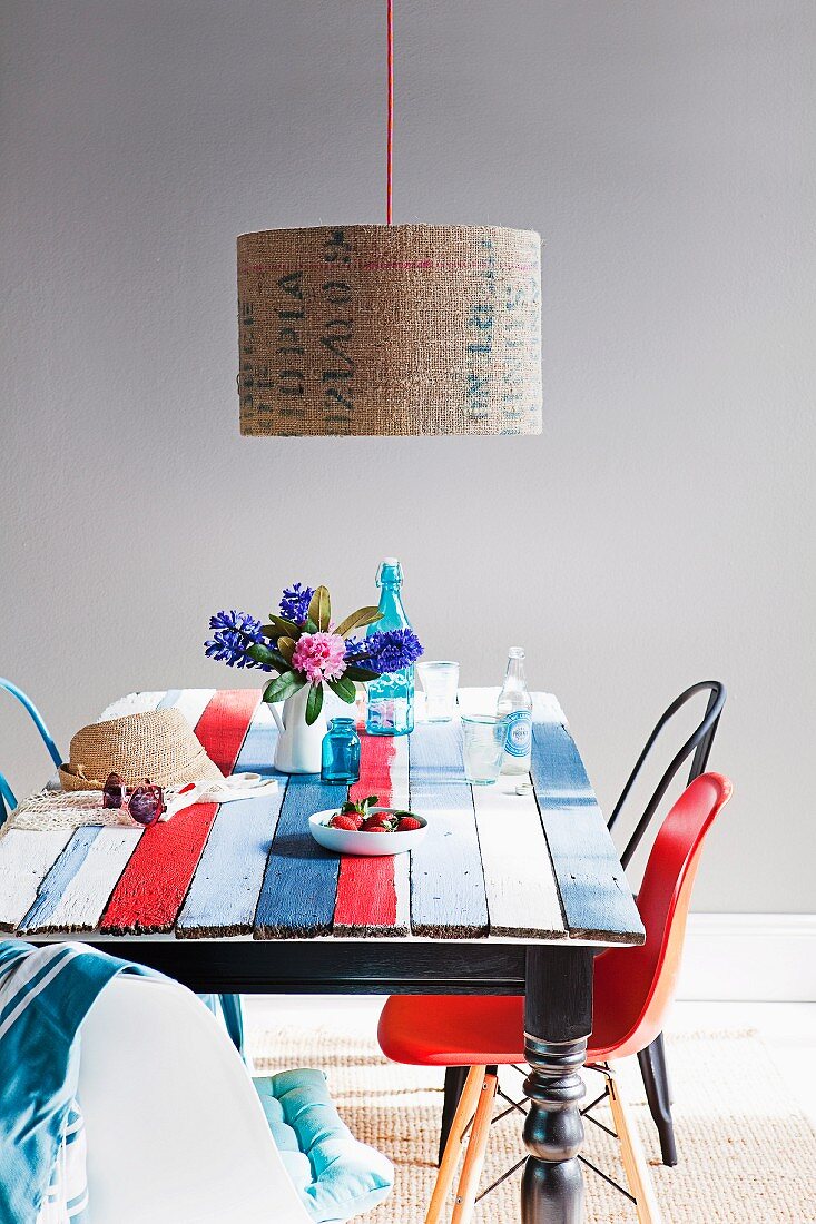 Antique table with old board top painted in new, striped maritime colours complemented by lampshade with printed lettering and collection of vintage chairs