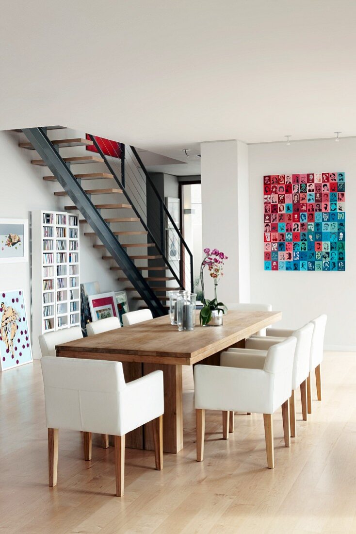 weiße gepolsterte Stühle an modernem Holz Esstisch gegenüber moderner Photogalerie an Wand in offenem Wohnraum mit Treppenaufgang
