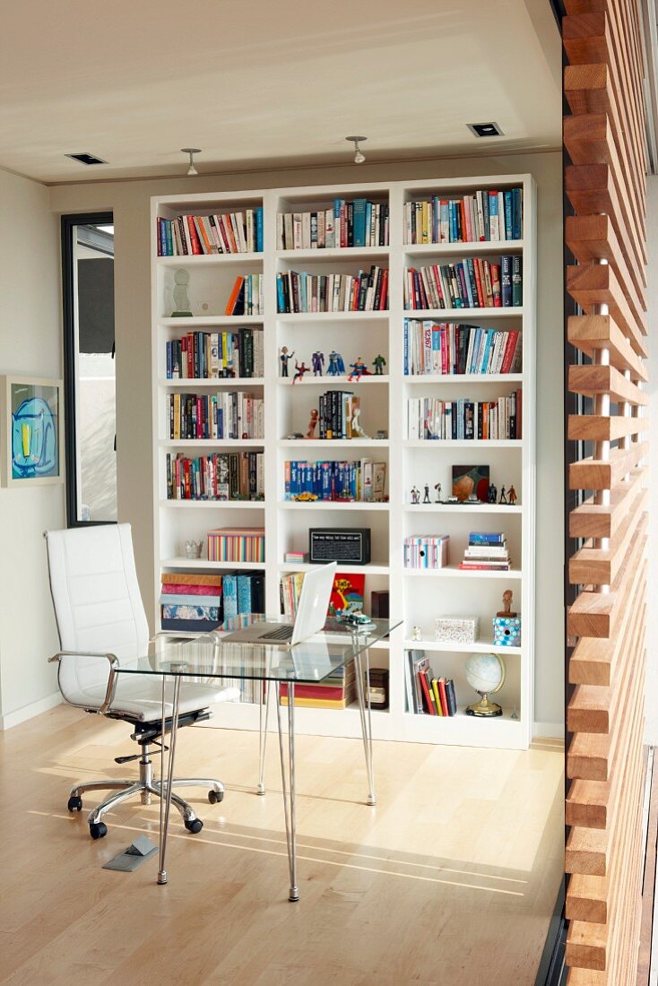 Modern workspace - glass table with metal frame and white office chair in front of white bookcase against wall