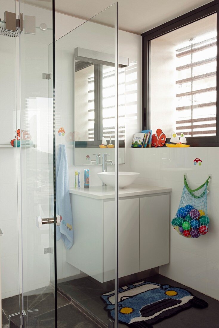 Verglaster Duschbereich neben Waschtisch mit weißem Unterschrank in Badezimmerecke unter dem Fenster