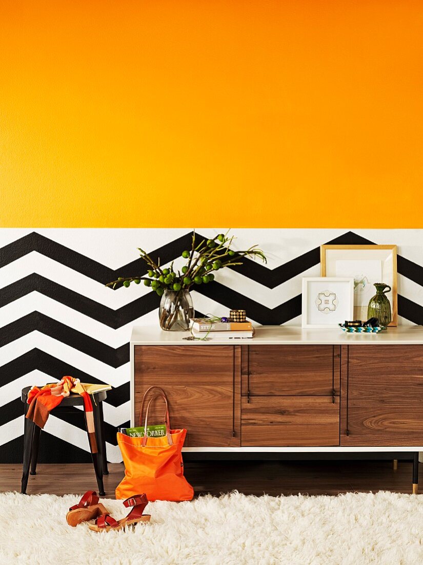 Orangegelber Farbverlauf über schwarzweissem Zickzacksockel als bewegter Hintergrund für Designer Sideboard