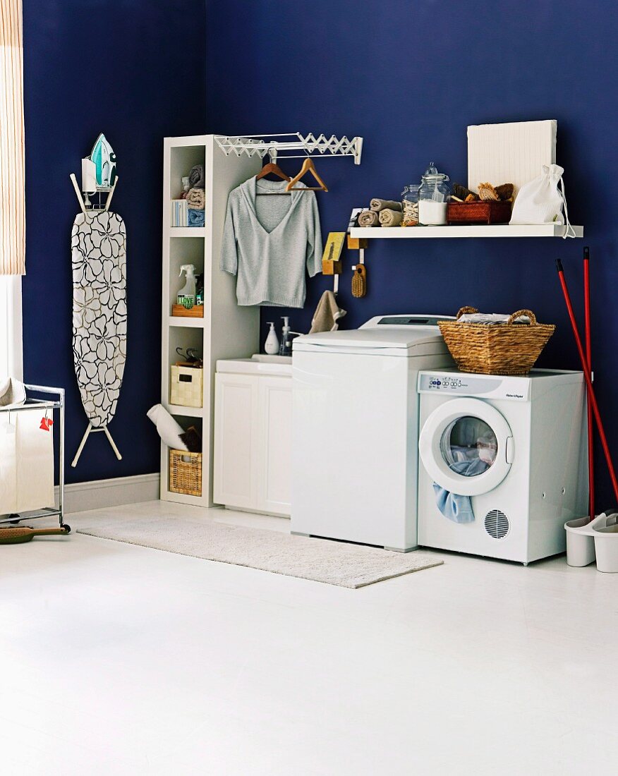 Blaue Waschküche mit Waschmaschine, Trockner und einer an der Wand hängenden Bügelstation