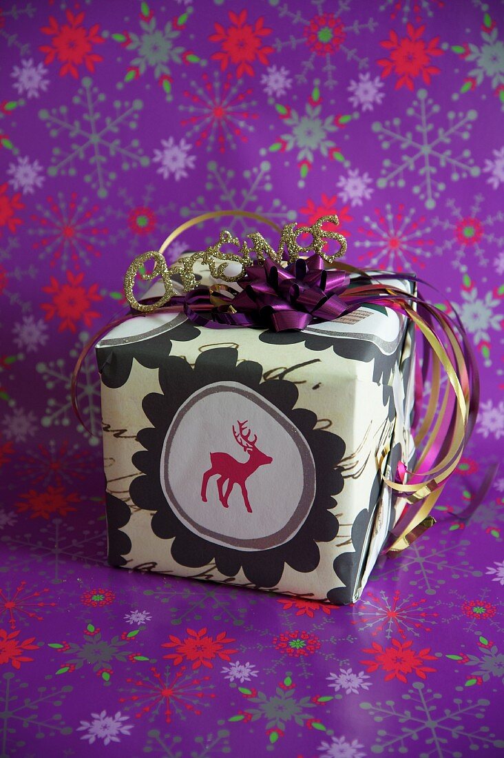 Verpacktes Weihnachtsgeschenk mit Rentiermotiv auf violettem Geschenkpapier mit Sternenmuster