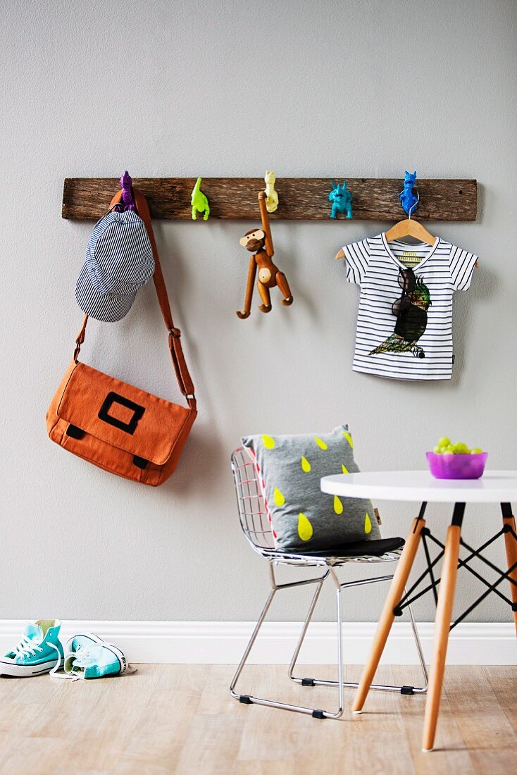 Rustikaler Holz Garderobenleiste mit Haken aus Spielzeugfiguren an Wand; Tisch und Bauhaus-Stuhl