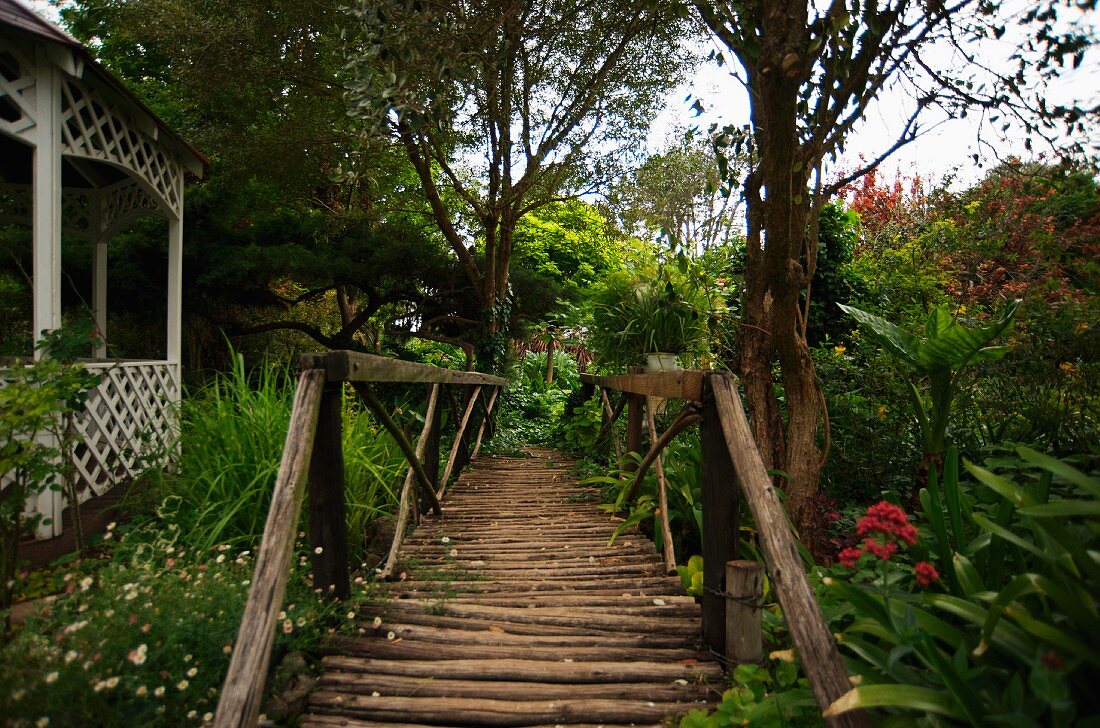 Romantische, alte Holzbrücke neben Pavillon in dicht bewachsenem Garten