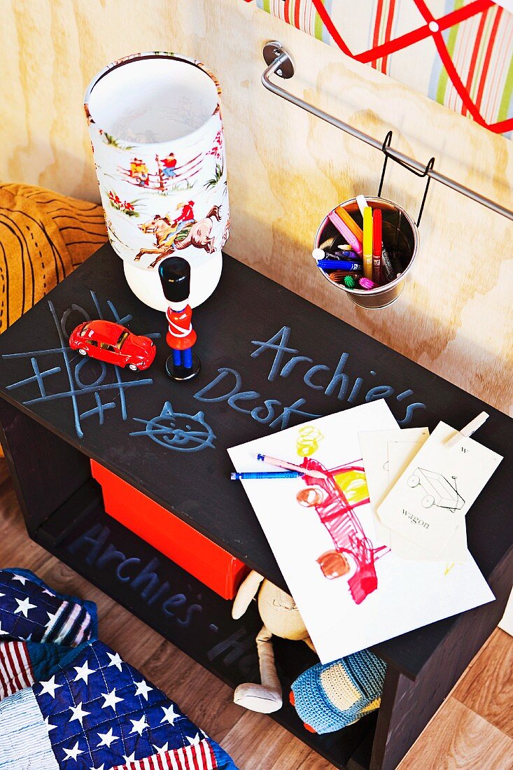 Bedside table with chalkboard top, lamp, children's drawings and toys