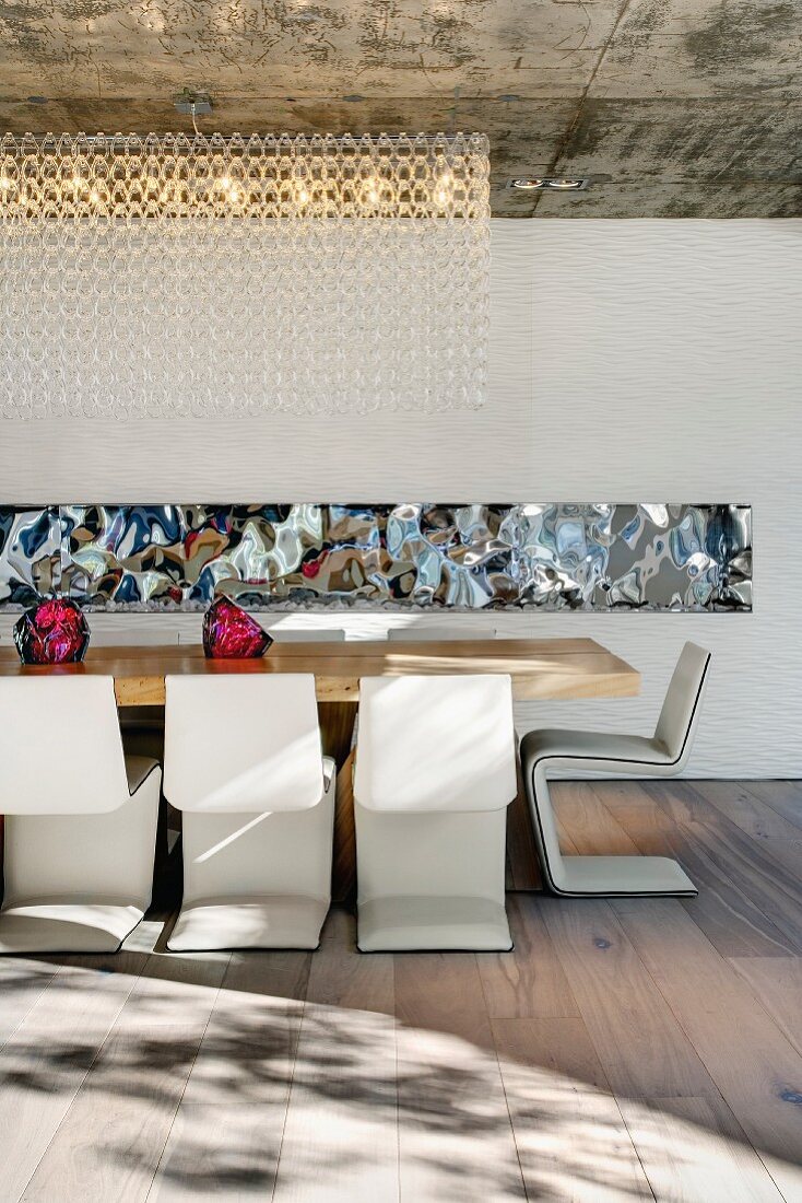 Designer dining area with cantilever chairs at a long table and mirror strips on the back wall; decorative lighting from the exposed concrete ceiling