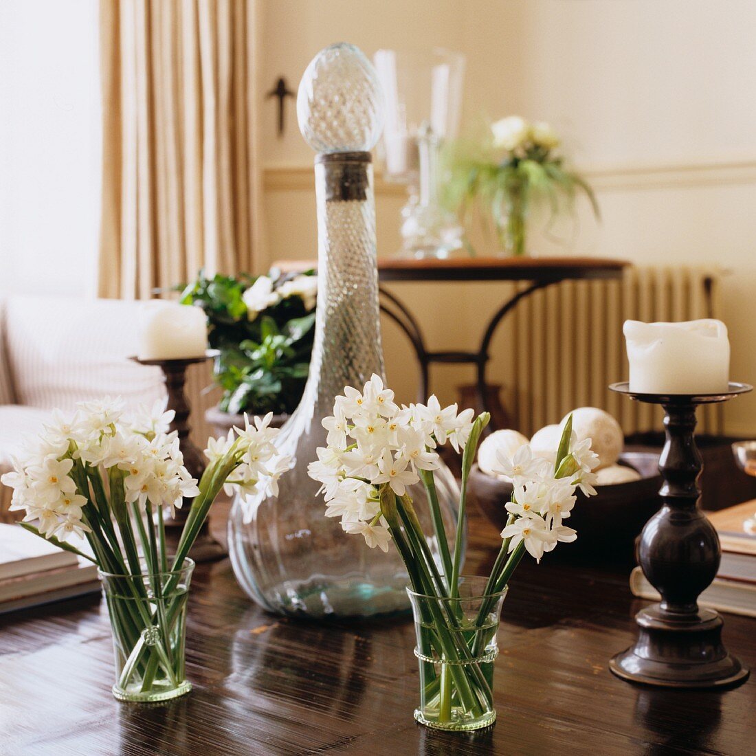 weiße Blumen im Glas vor antiker Karaffe und Kerzenständer auf Holztisch