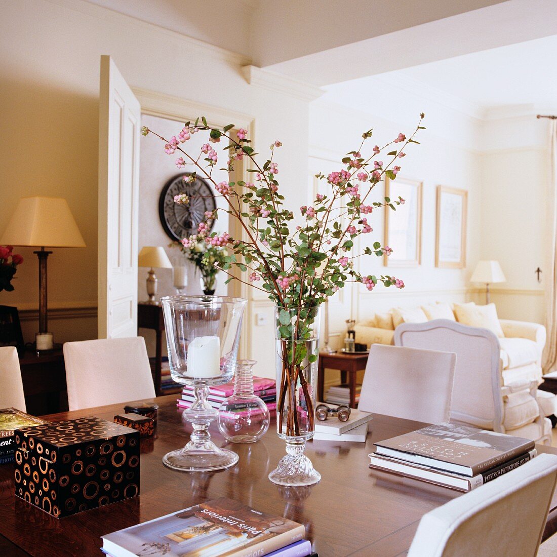 Zweig mit rosa Schneeberen in Vase zwischen Bücherstapeln auf Tisch in traditionellem Wohnzimmer