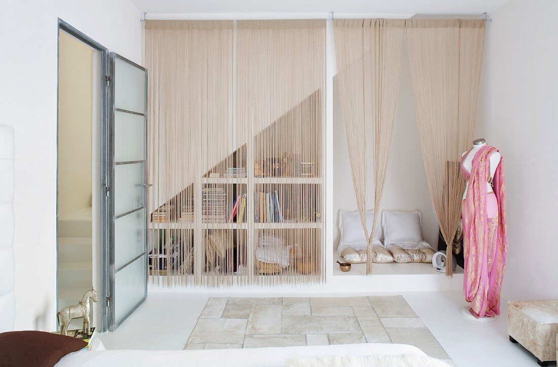 Künstlerisches Schlafzimmer mit Schnurvorhang vor einer Polstersitzecke unter der Treppenschräge; Schneiderpuppe mit drapiertem Stoff