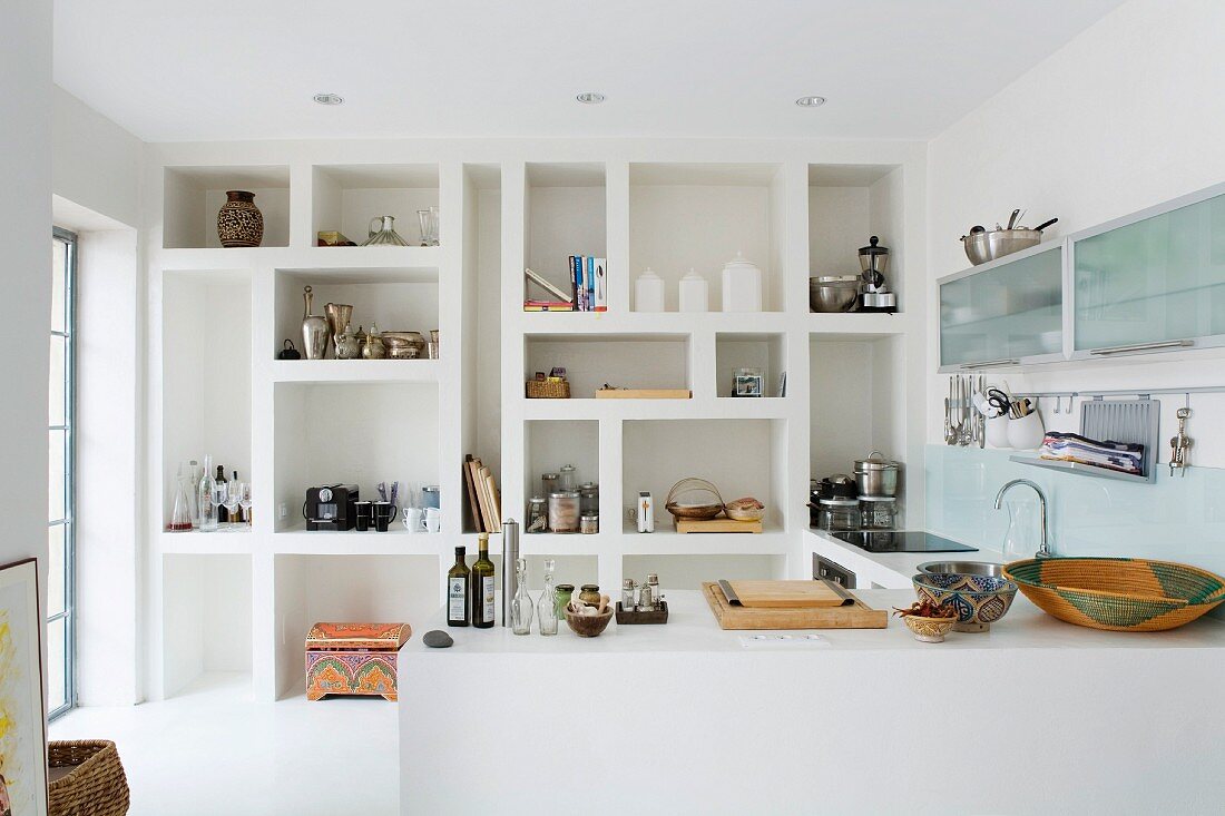 Large-scale fitted shelving with irregular compartments in minimalist white kitchen