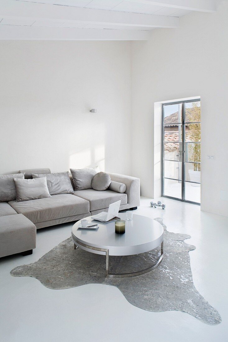Purist living room in grey and white with designer table on animal-skin rug and corner sofa