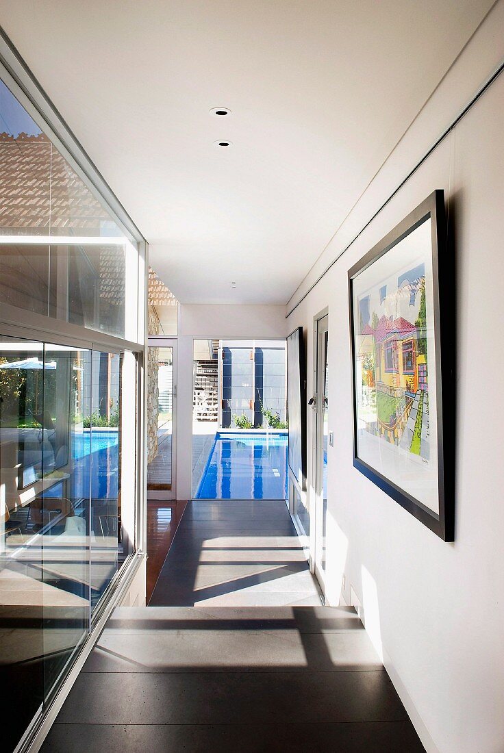 Sunny corridor with view of swimming pool; framed artworks on wall