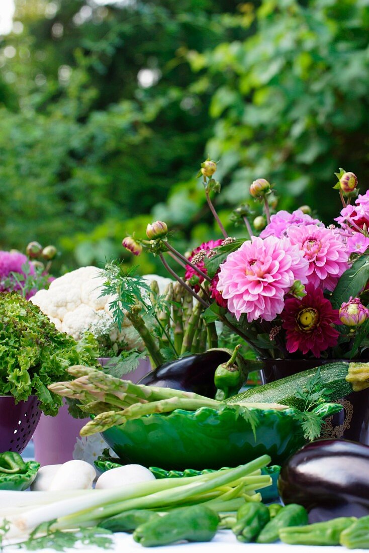 Gemüsepräsentation und farbenfroher Dahlienstrauss auf einem Tisch im Garten