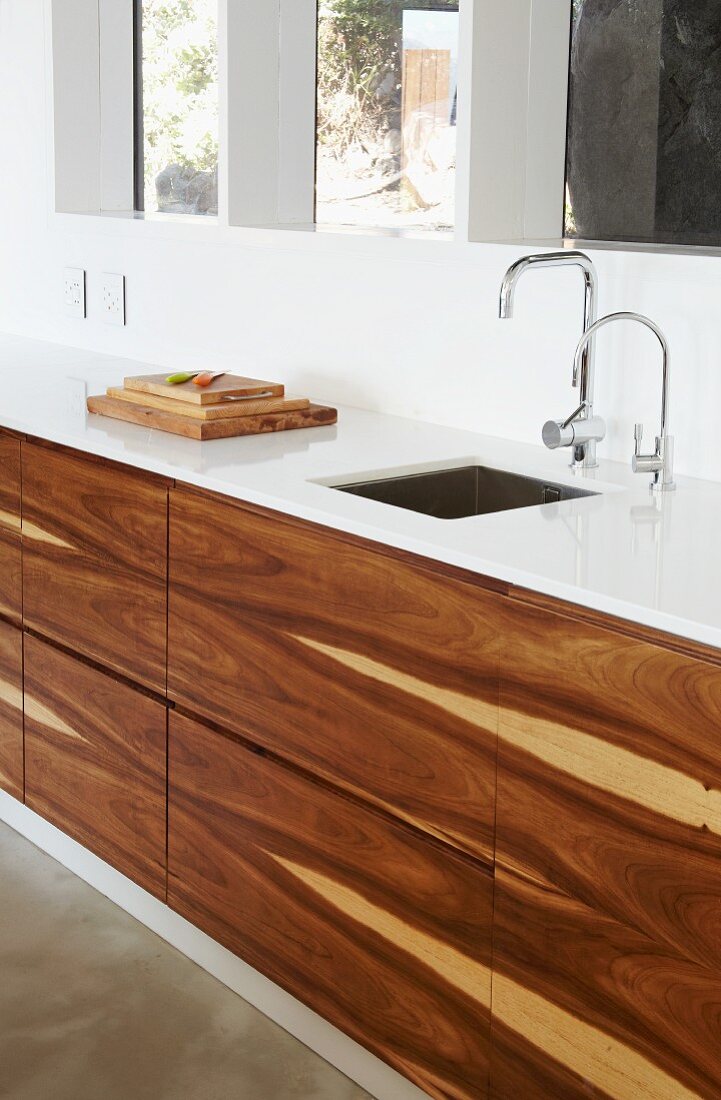 Designer kitchen counter with white worksurface and base unit fronts of tropical wood