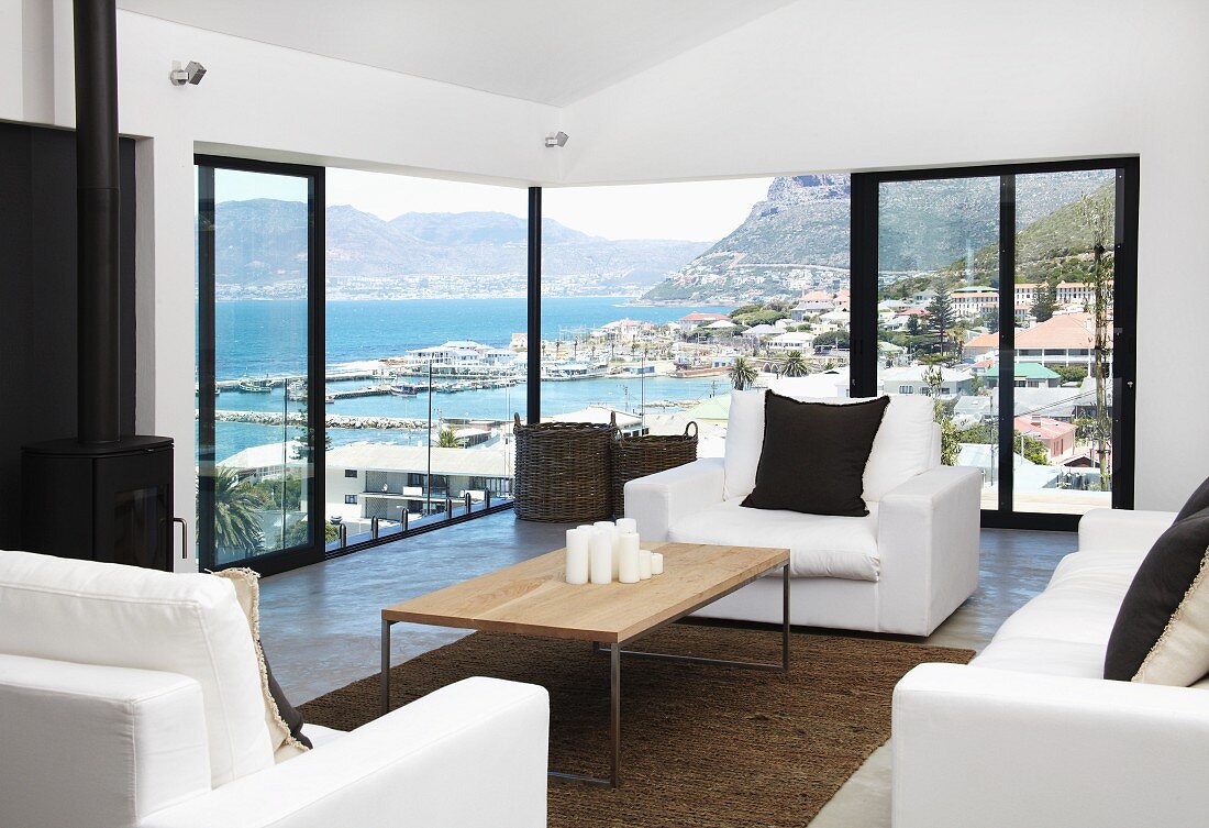 Wohnraum mit Panoramablick auf bergige Meeresküste - Couchtisch mit Holzplatte und weiße Polstersofagarnitur