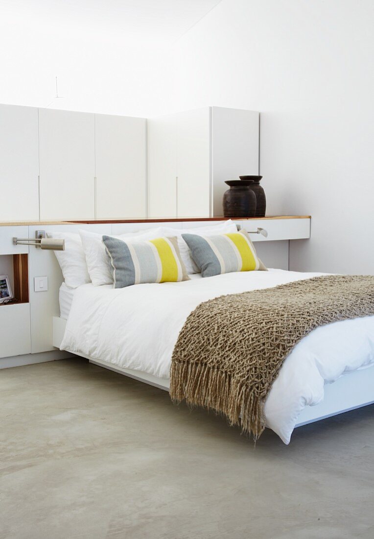Modernes Doppelbett mit Tagesdecke vor Raumteiler in Schlafbereich