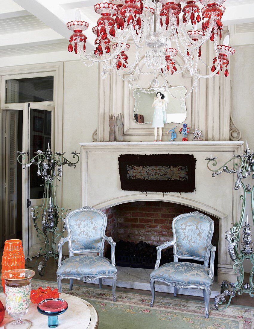 Silver gilt, antique armchairs with shimmering upholstery and chandelier with red crystals in front of open fireplace