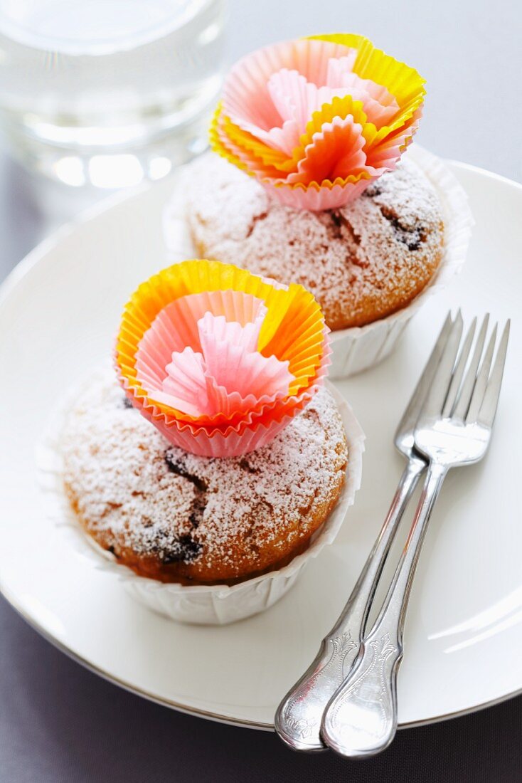 Muffins, verziert mit Papierblüten aus Muffinförmchen