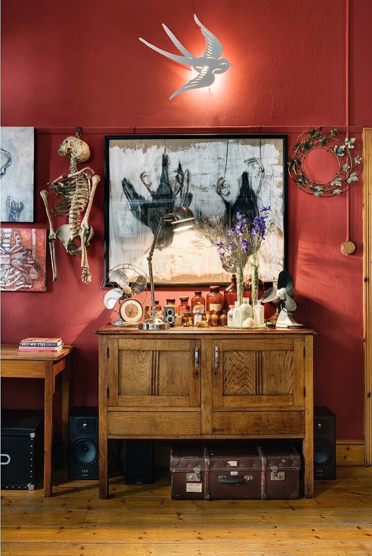 Swallow-shaped sconce lamp on wall above collection of bizarre objets d'art and vintage cabinet