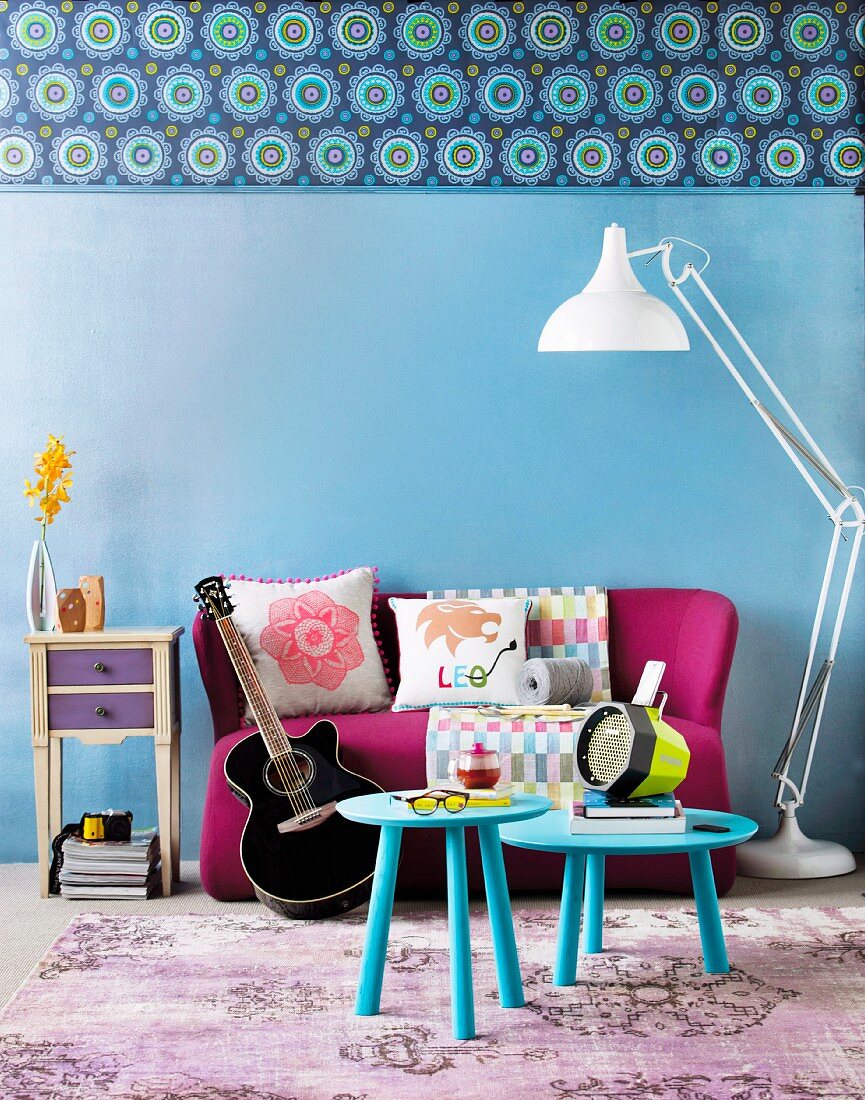 Modernes Sofa und Beistelltische in kräftigen Farben, kombiniert mit neutraler Stehlampe und hell gemusterten Kissen