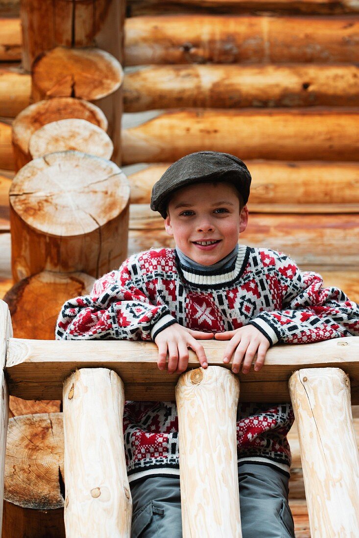 Young boy leaning on a wooden railing in front of a log cabin