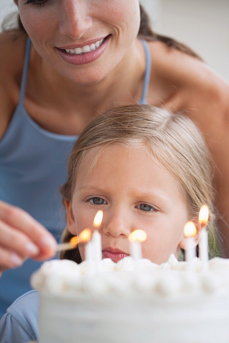 Mother lighting the candles on her daughter's birthday cake