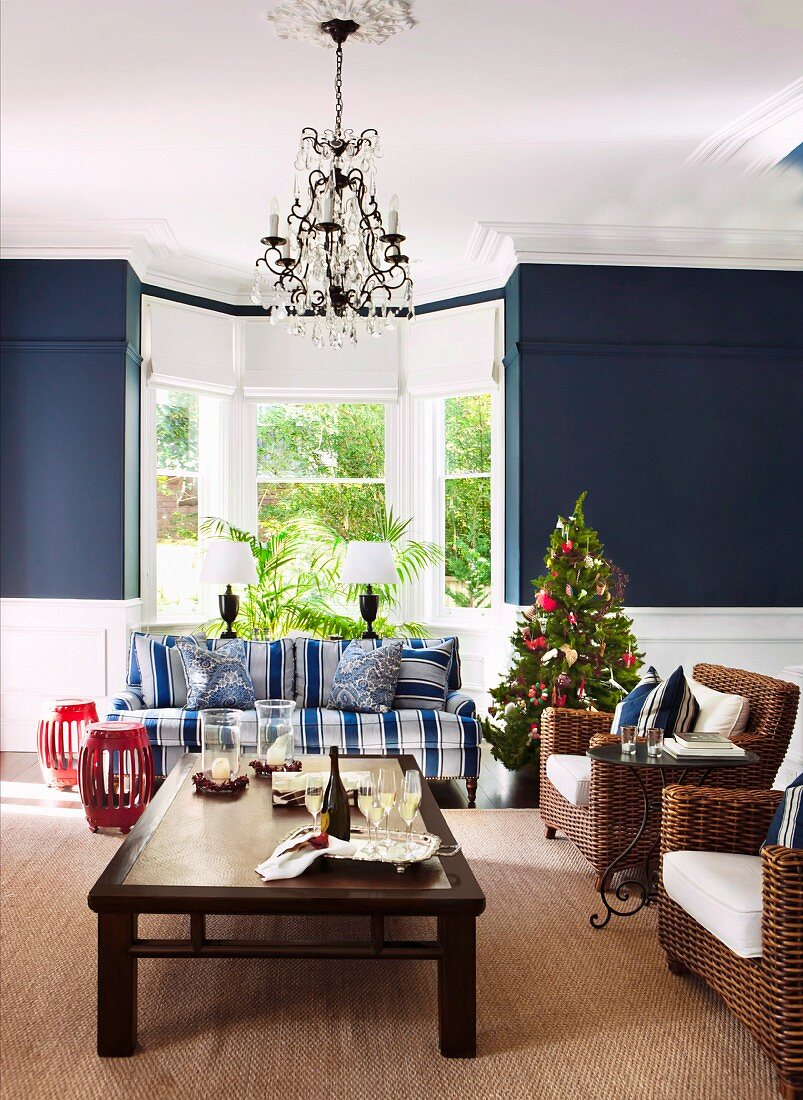 Kleiner Weihnachtsbaum zwischen blauweiss gestreiftem Sofa und Korbsesseln vor Wohnraumerker mit blau getönten Seitenwänden