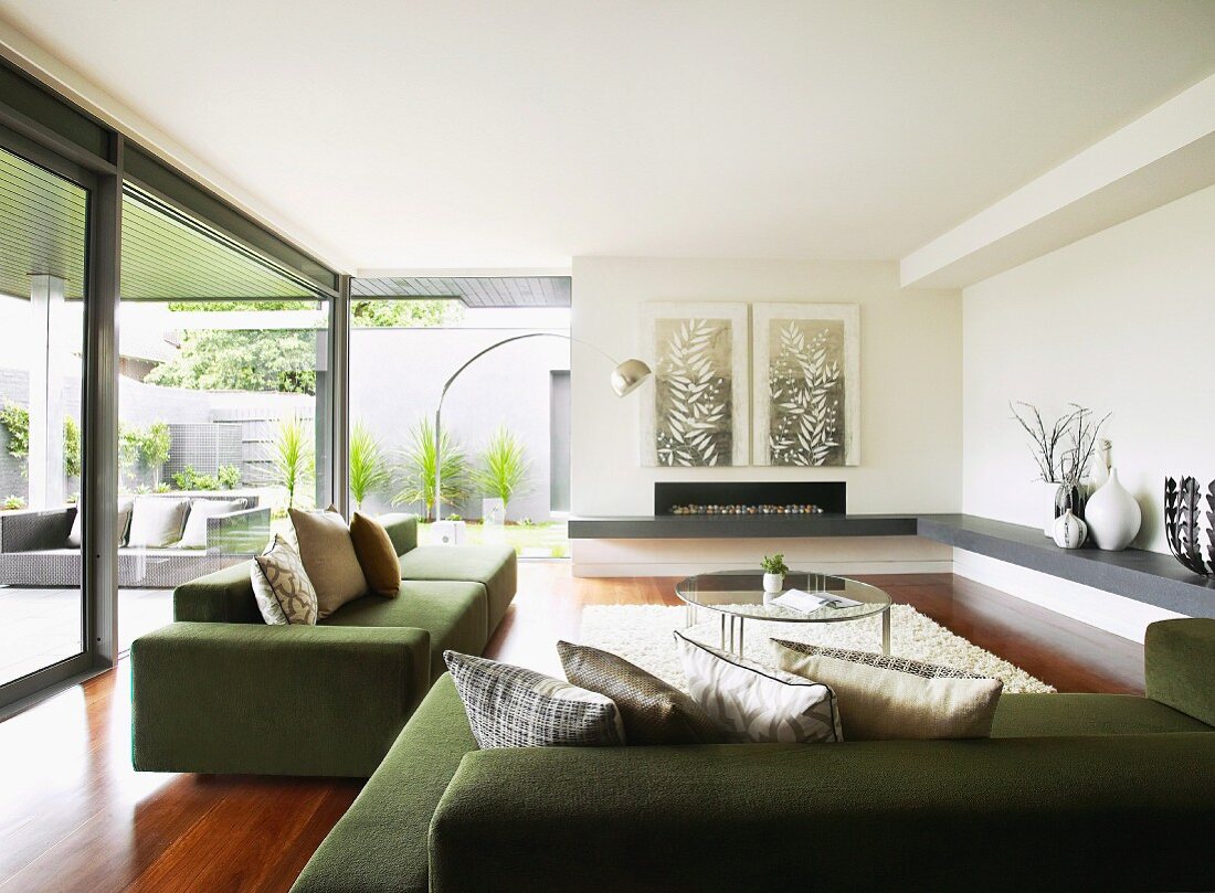 Moderne grüne Sofagarnitur mit drapierten Kissen in grosszügigem Wohnraum und Blick in Patio