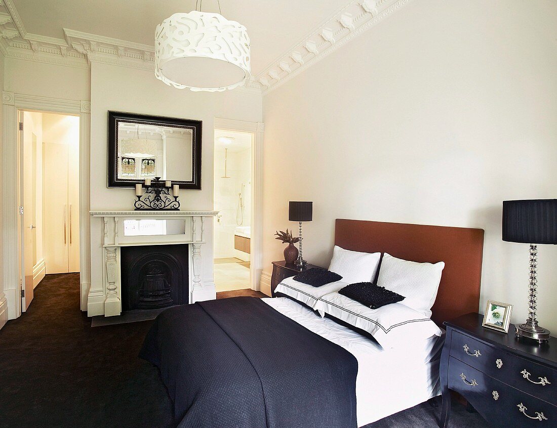 Doppelbett mit gepolstertem Kopfteil und dunkelblauer Tagesdecke in traditionellem Schlafzimmer mit offenem Kamin