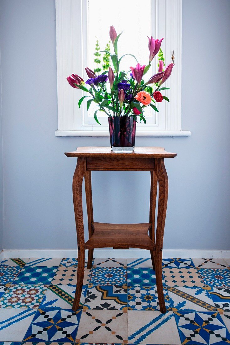Bouquet of lilies on retro side table standing on floor tiles with various Oriental patterns