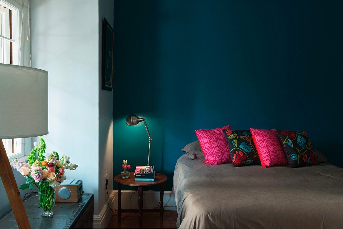 Scatter cushions on double bed and bedside table against petrol blue wall