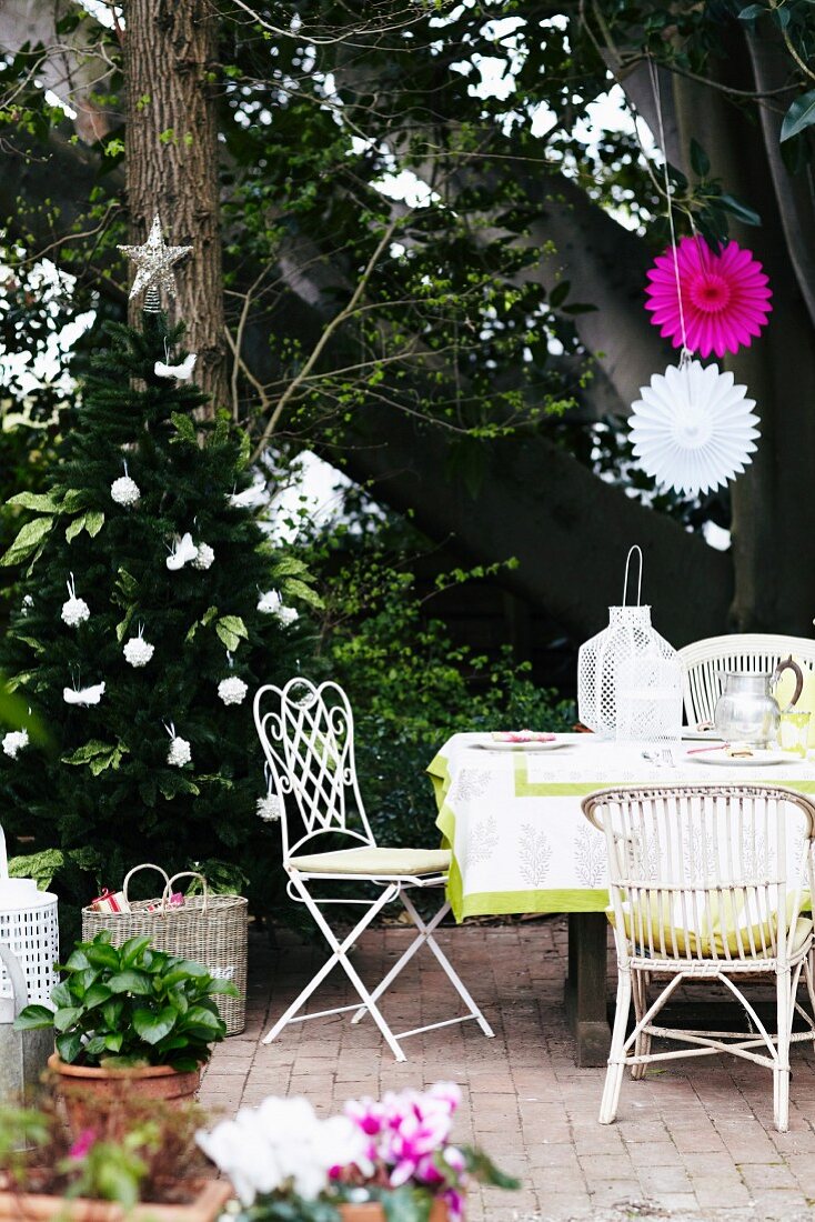 Festively decorated terrace with set terrace table and white chairs; potted flowering plants in foreground