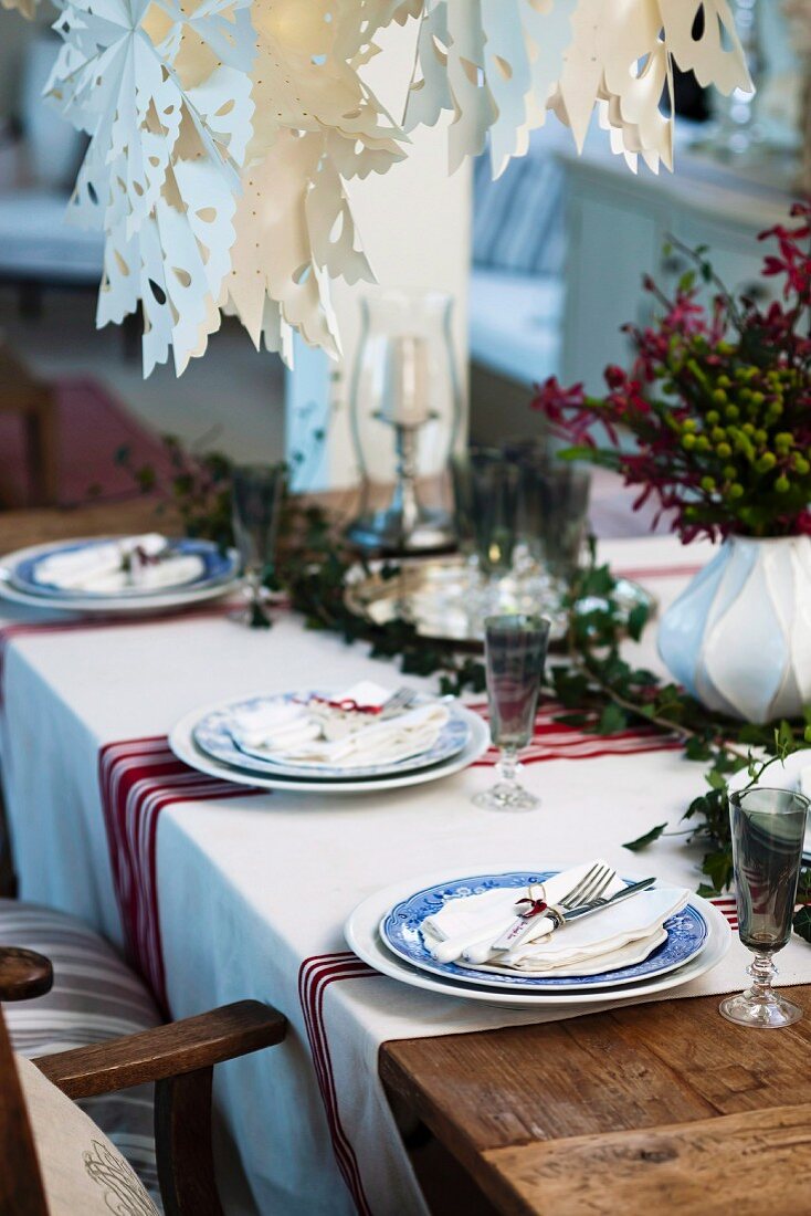 Im Landhausstil weihnachtlich gedeckter Tisch mit rotweiss gestreiftem Tischläufer und kunstvollen Adventssternen aus weißem Papier