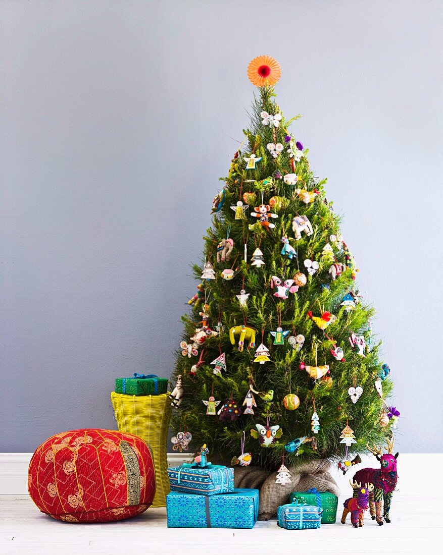 Red pouffe, wrapped presents and animal ornaments under Christmas tree decorated with many different figurines