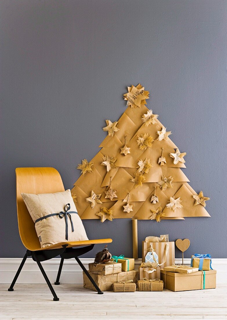 Christmas presents below stylised Christmas tree made from paper triangles with paper Christmas decorations on grey wall