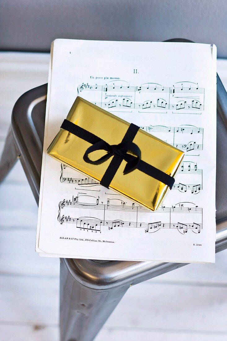 Book of sheet music and present wrapped in gold paper with black ribbon on metal stool