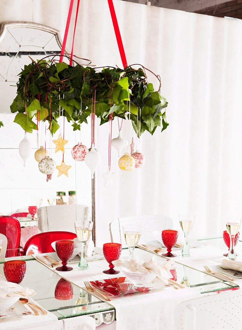 Wreath decorated with Christmas baubles suspended from ceiling above set table with red, retro wine glasses
