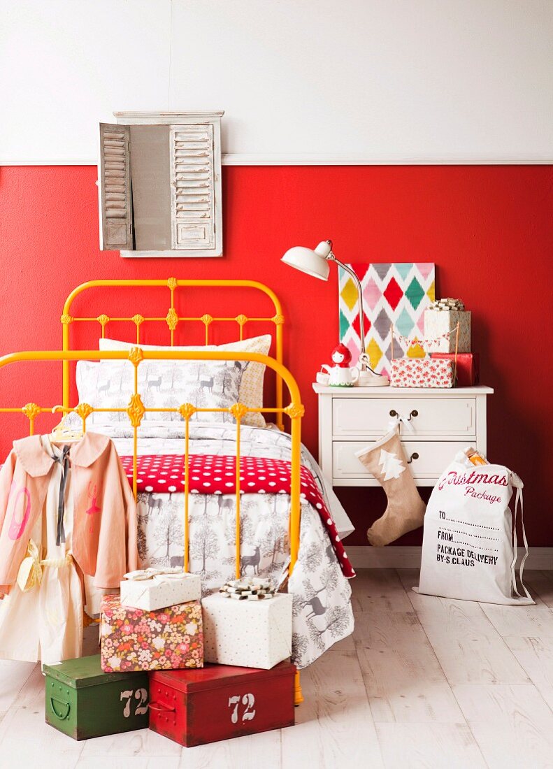 Parcels on white wooden floor next to single bed with yellow-painted metal frame and bedside table against wall with red, painted dado