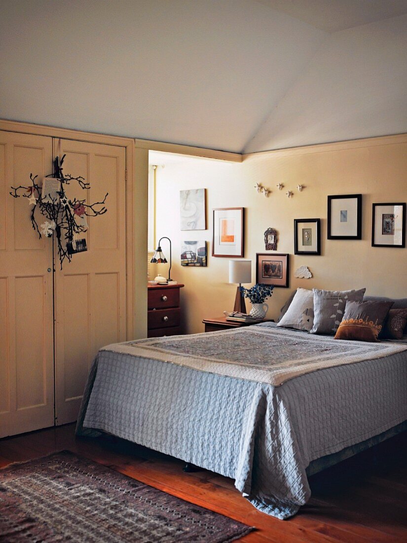 Floral decoration on wardrobe doors and gallery of pictures on wall above double bed in country-house bedroom