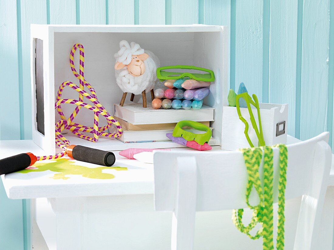 Toys on small table and white chair in front of turquoise wooden wall