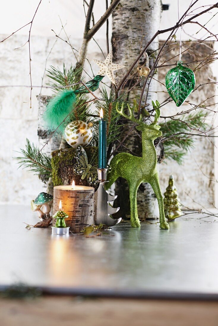 Grüne Rentierfigur und brennende Kerzen vor weihnachtlich dekoriertem Baumstamm