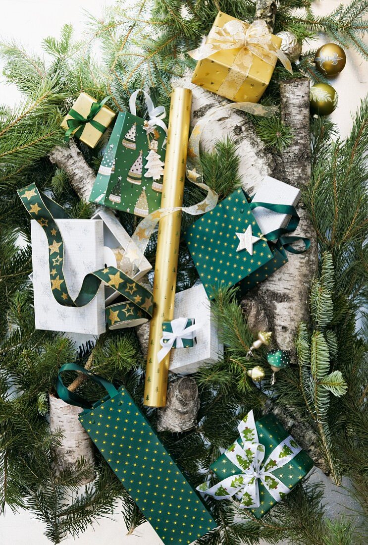 Kleine Geschenktüten und Päckchen mit Weihnachtsmotiven auf Tannenzweigen und Baumstämmen