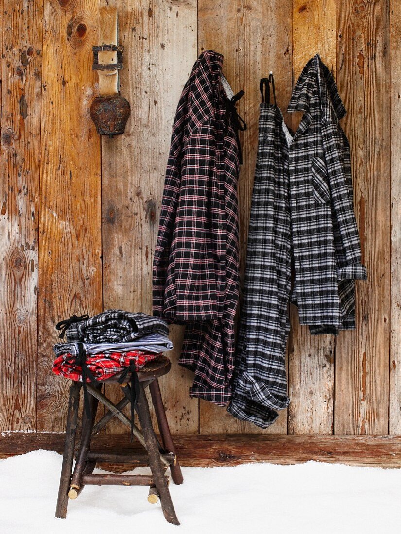 Kleidung auf rustikalem Hocker vor Holzwand mit aufgehängten Pyjamas im Karolook an Wandhaken