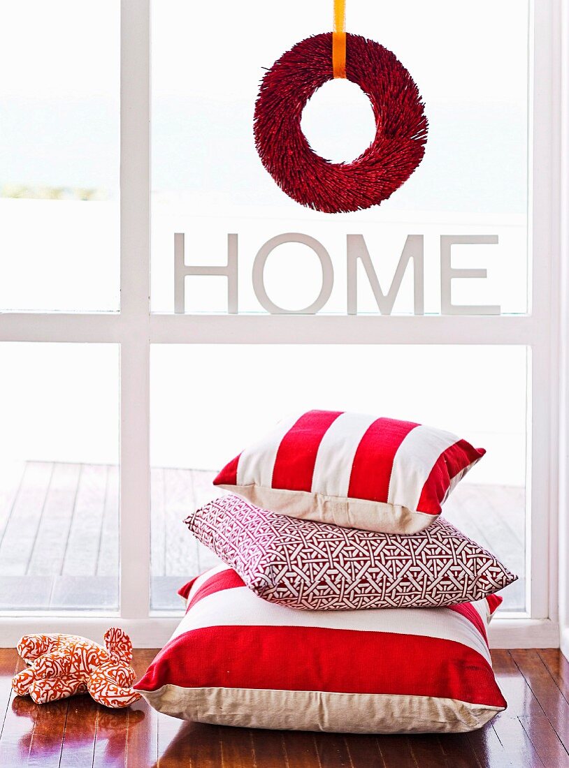 Festive wreath made from red feather boa in window above pile of scatter cushions